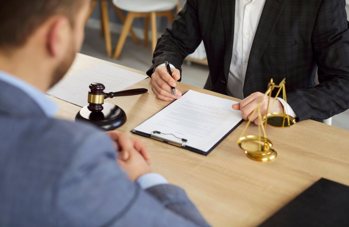 Male lawyer discussing contract with man client going to sign documents in office. Attorney having a meeting sitting at desk with a judge's gavel and scales. Legal law and advice concept.